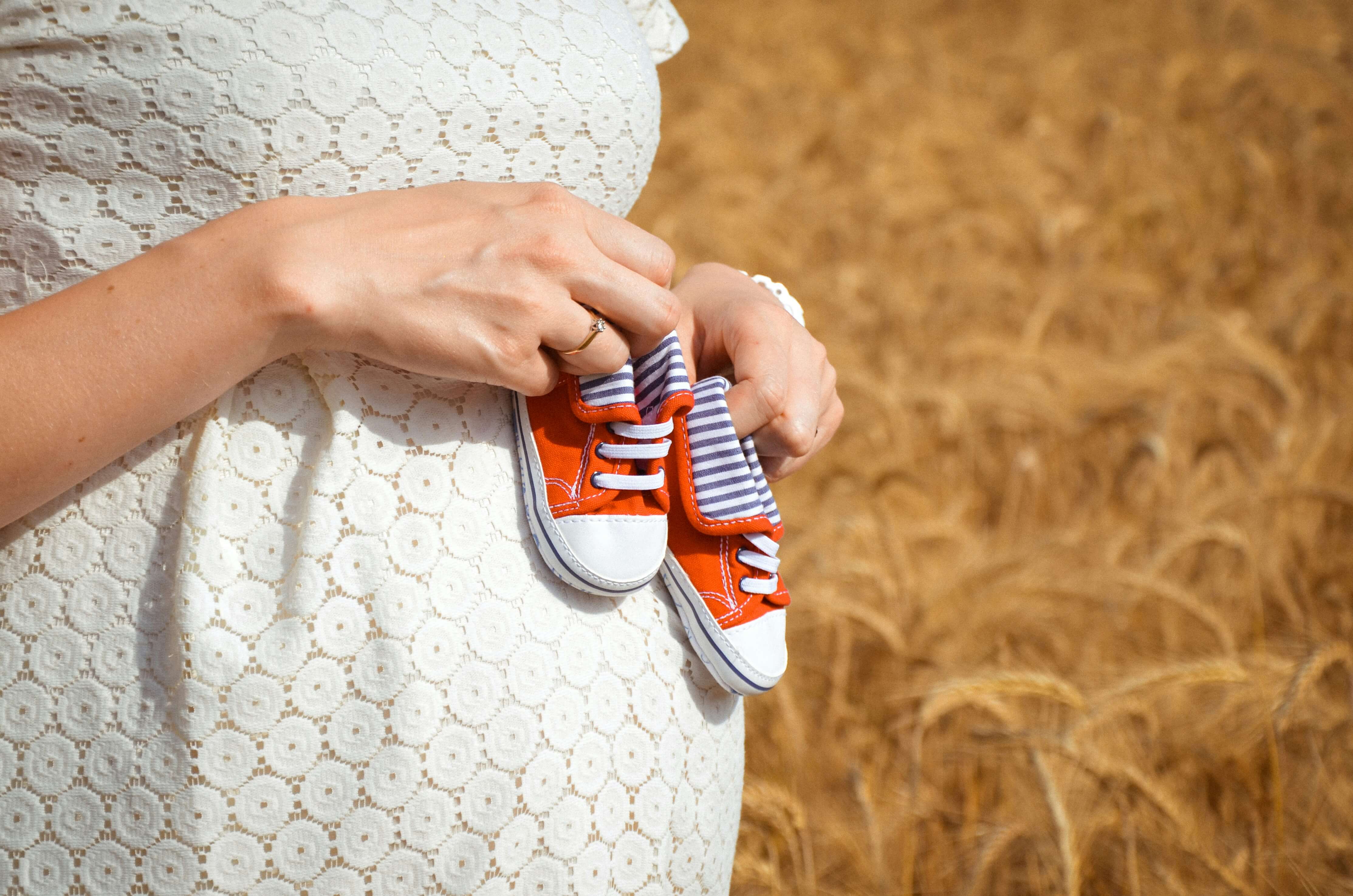 Schwangere Person hält kleine Babyschuhe vor dem Bauch